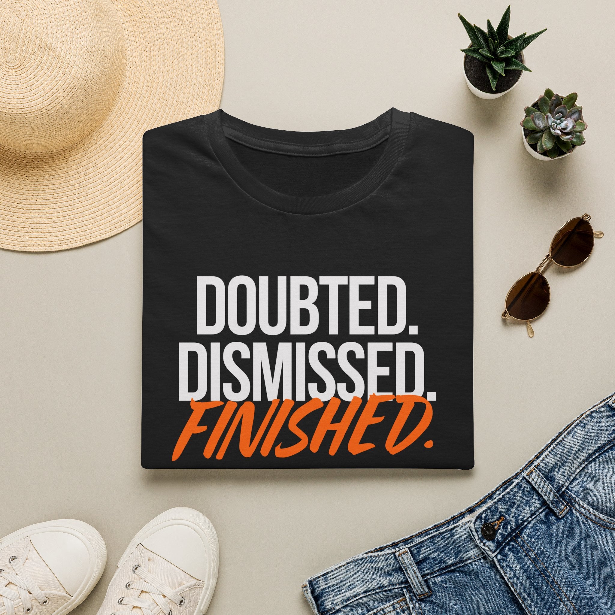 Black t-shirt with 'Doubted. Dismissed. Finished.' text, surrounded by casual items on a light surface.