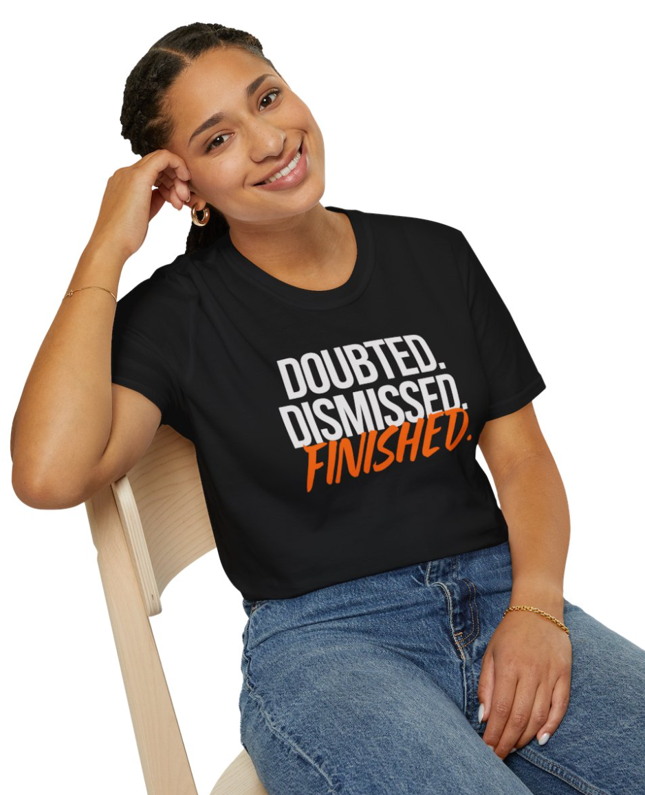 Woman wearing a black t-shirt with 'DOUBTED. DISMISSED. FINISHED.' text, sitting on a chair.